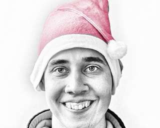 Ein Mann mit einem rosa Weihnachtsmannhut lächelt freundlich.