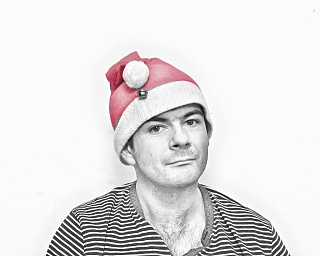 Porträt eines Mannes in Weihnachtsmütze vor weißem Hintergrund.