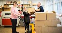 Drei Personen arbeiten zusammen in einem Lager mit Kartons.